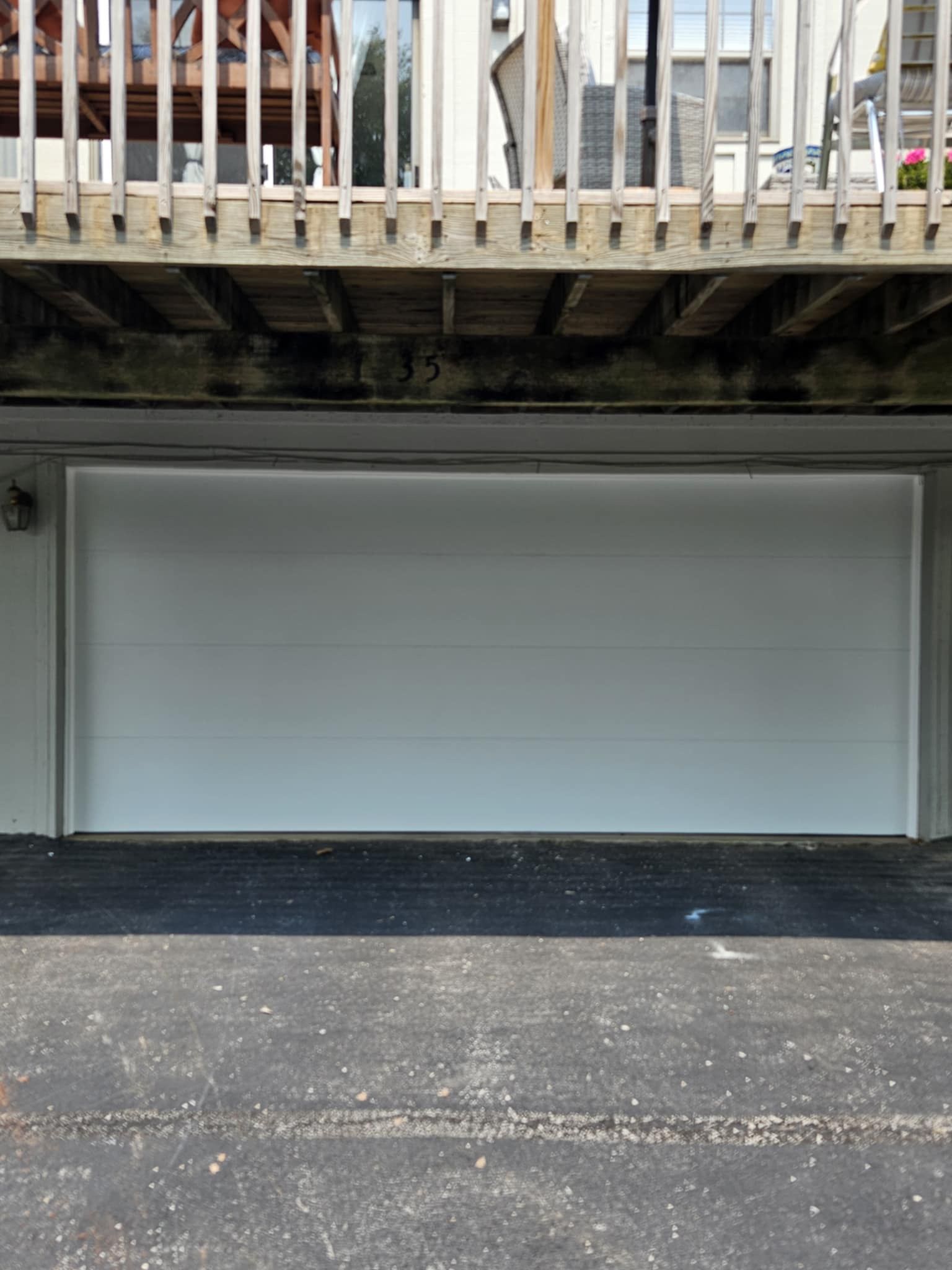 A white garage door is sitting under a deck next to a house.