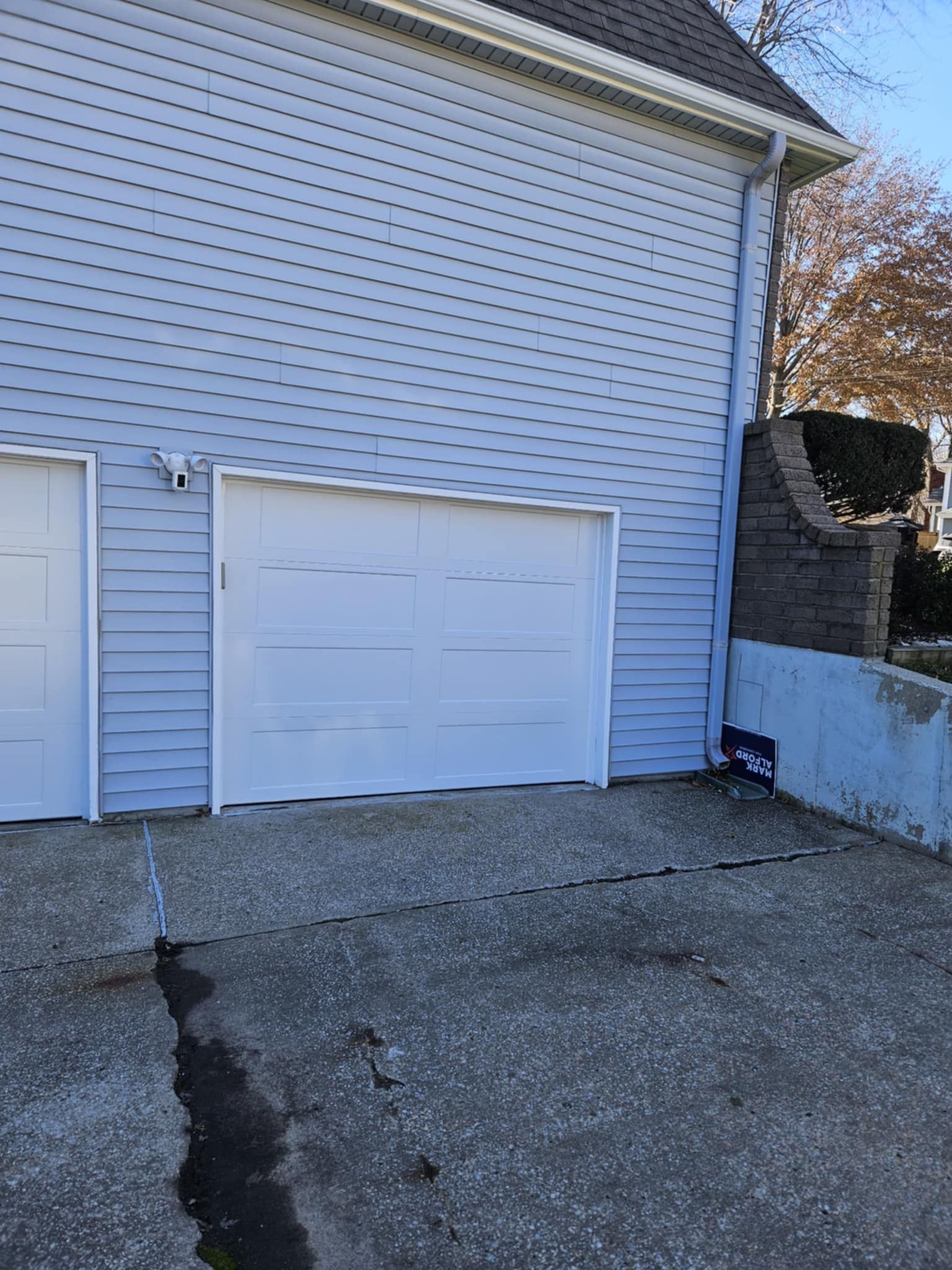 A white garage door is sitting next to a white house.
