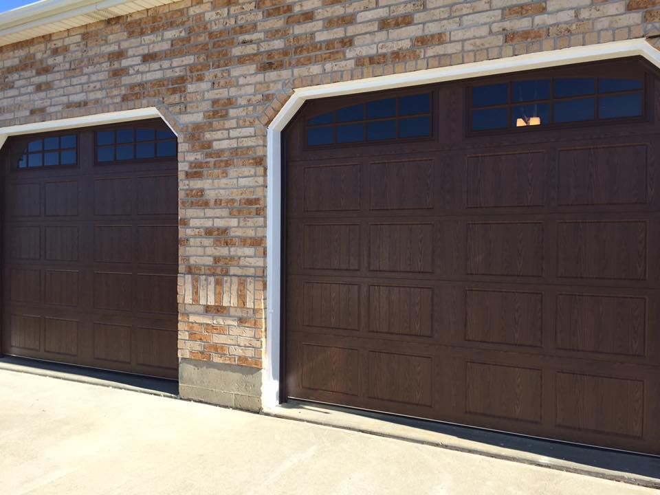 Two brown garage doors are on a brick building.