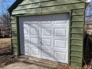 A garage with a white garage door and green siding. The garage door is new, white, & clean.
