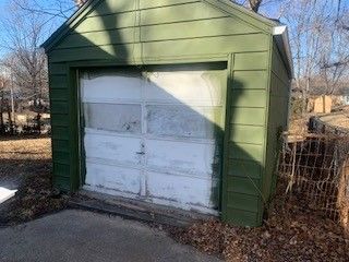 A green shed with a white garage door. The garage door is old, dirty, and has extra green paint on the edges.