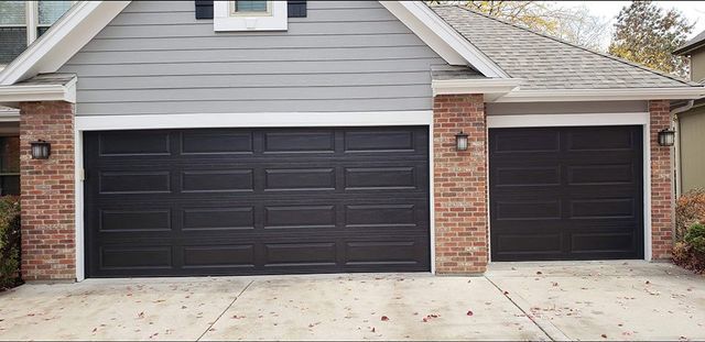There are two black garage doors on the side of a house.