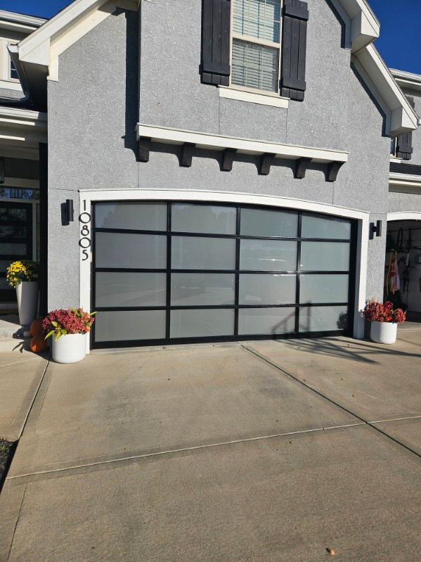 A large garage door is sitting in front of a gray house.