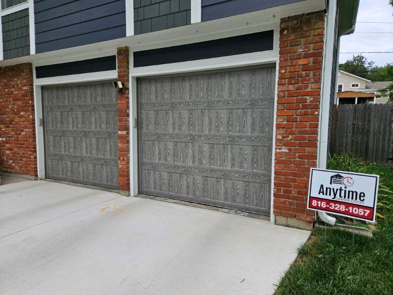 A brick house with two garage doors and a sign that says `` anytime ''.