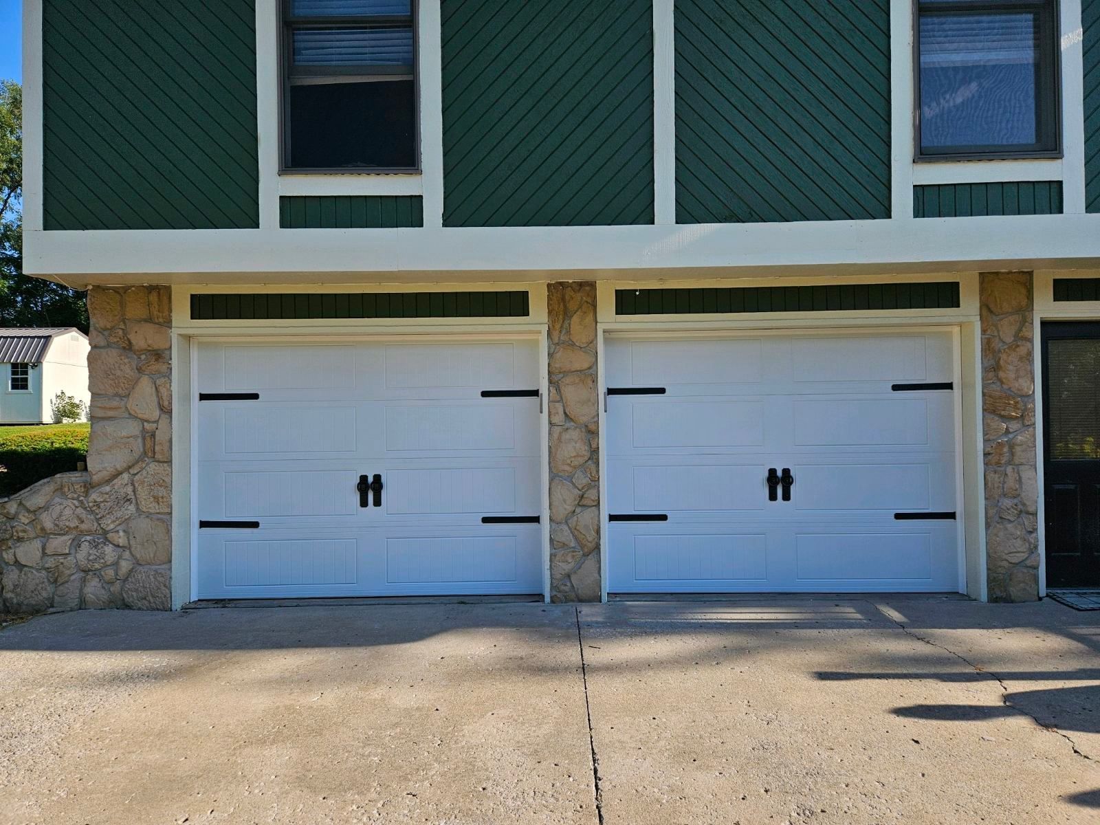 A green and white house with two white garage doors