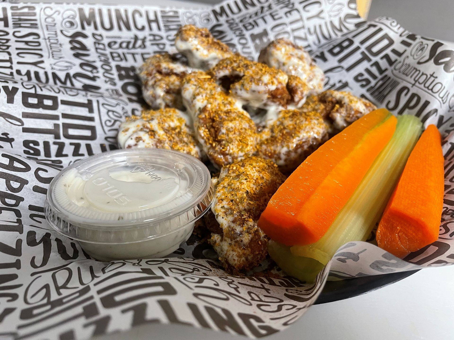 Chicken wings with dipping sauce and vegetables on a decorative paper in a basket.
