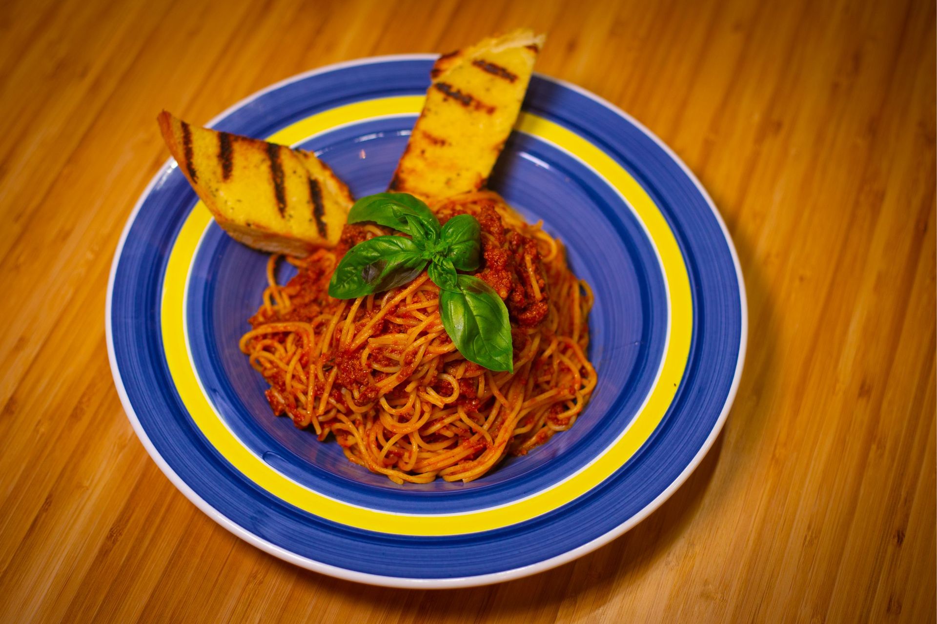 A blue plate topped with spaghetti and garlic bread on a wooden table.