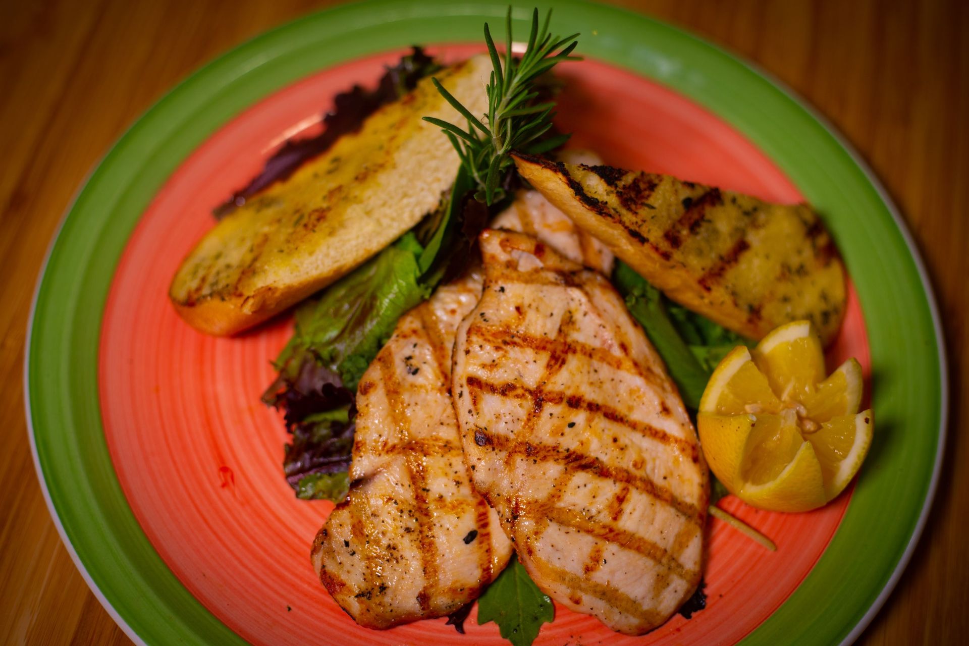 A green and pink plate topped with grilled chicken breasts and vegetables.