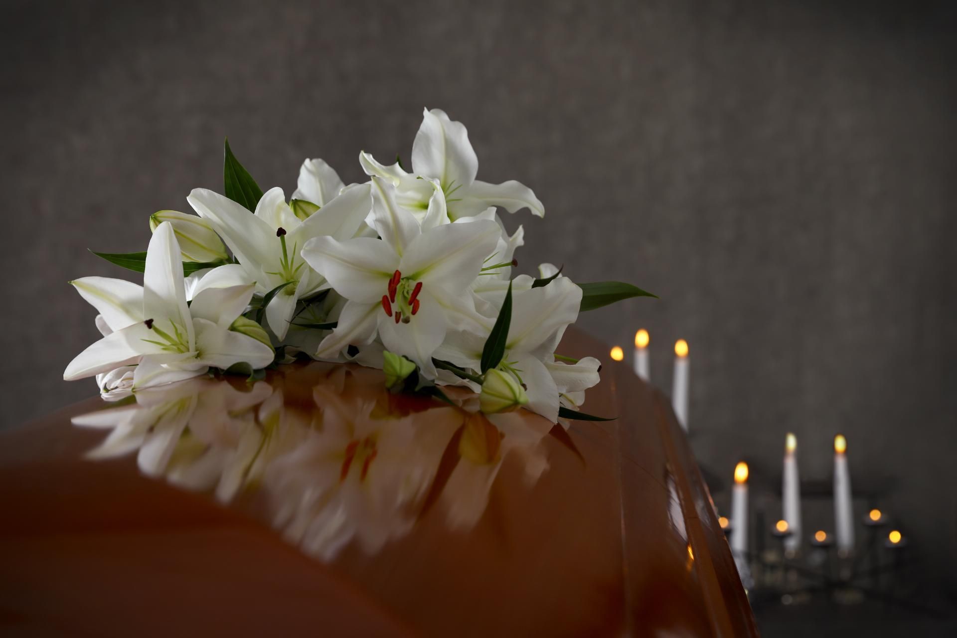 A coffin with white lilies and candles on it.