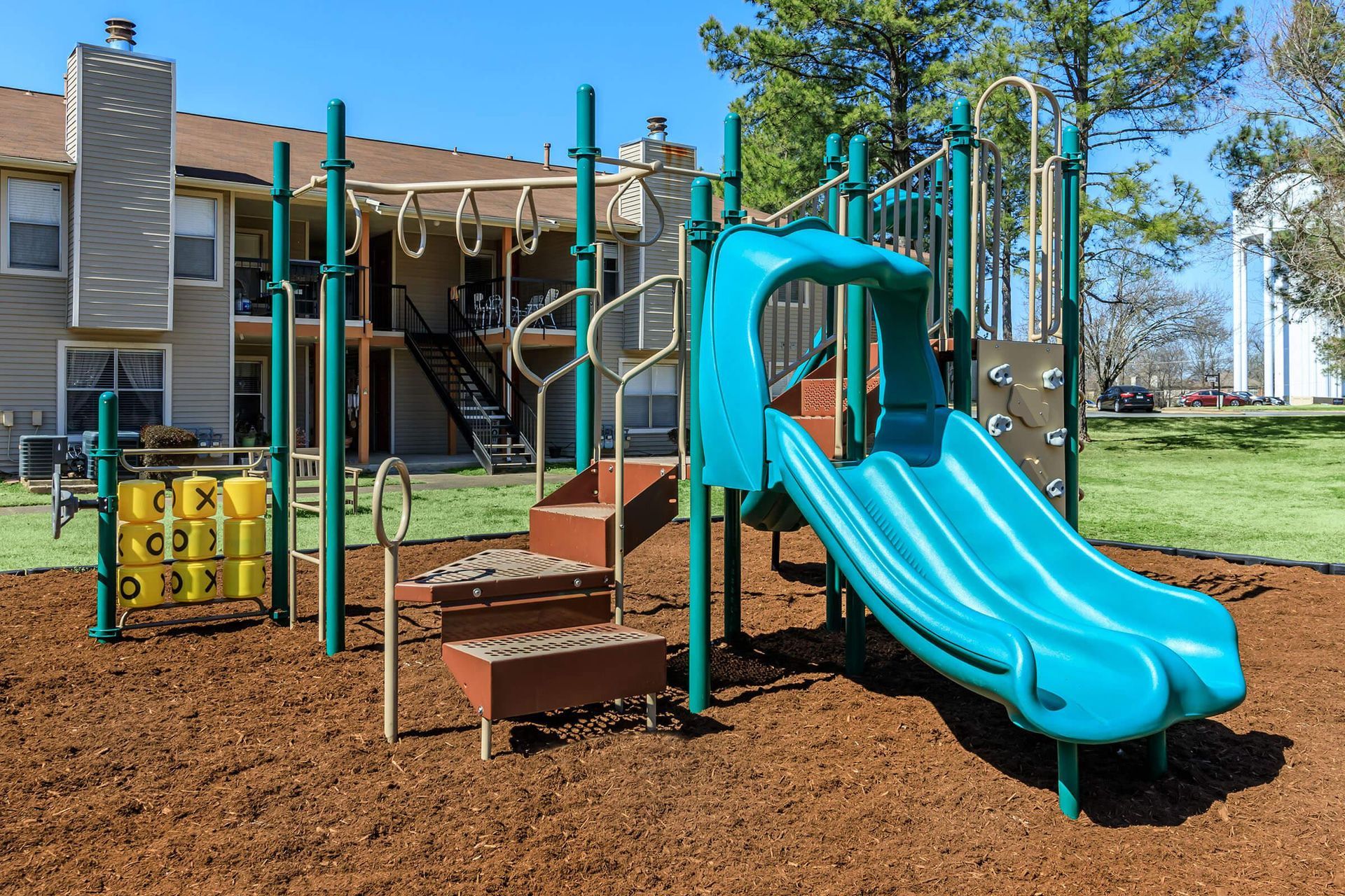 A blue slide is in a playground in front of a building at Overbrook Apartments.