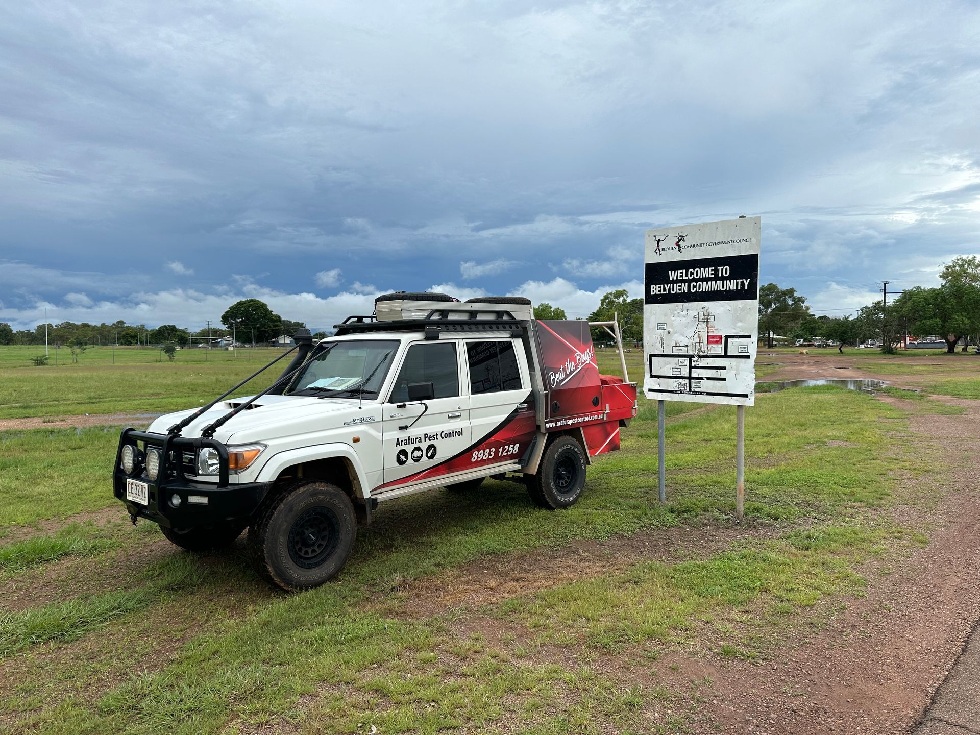 A white truck is parked in a grassy field next to a sign.