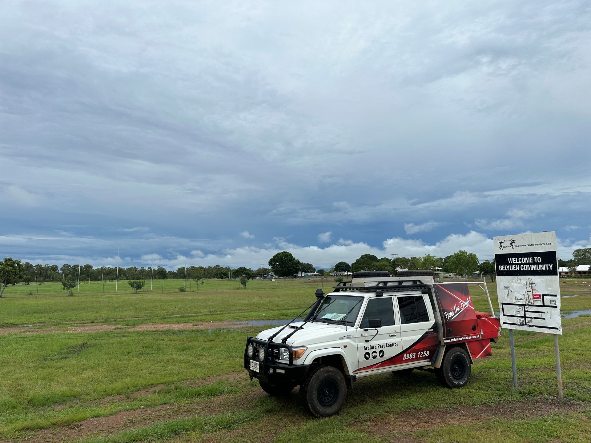 A white truck is parked in a grassy field next to a sign.