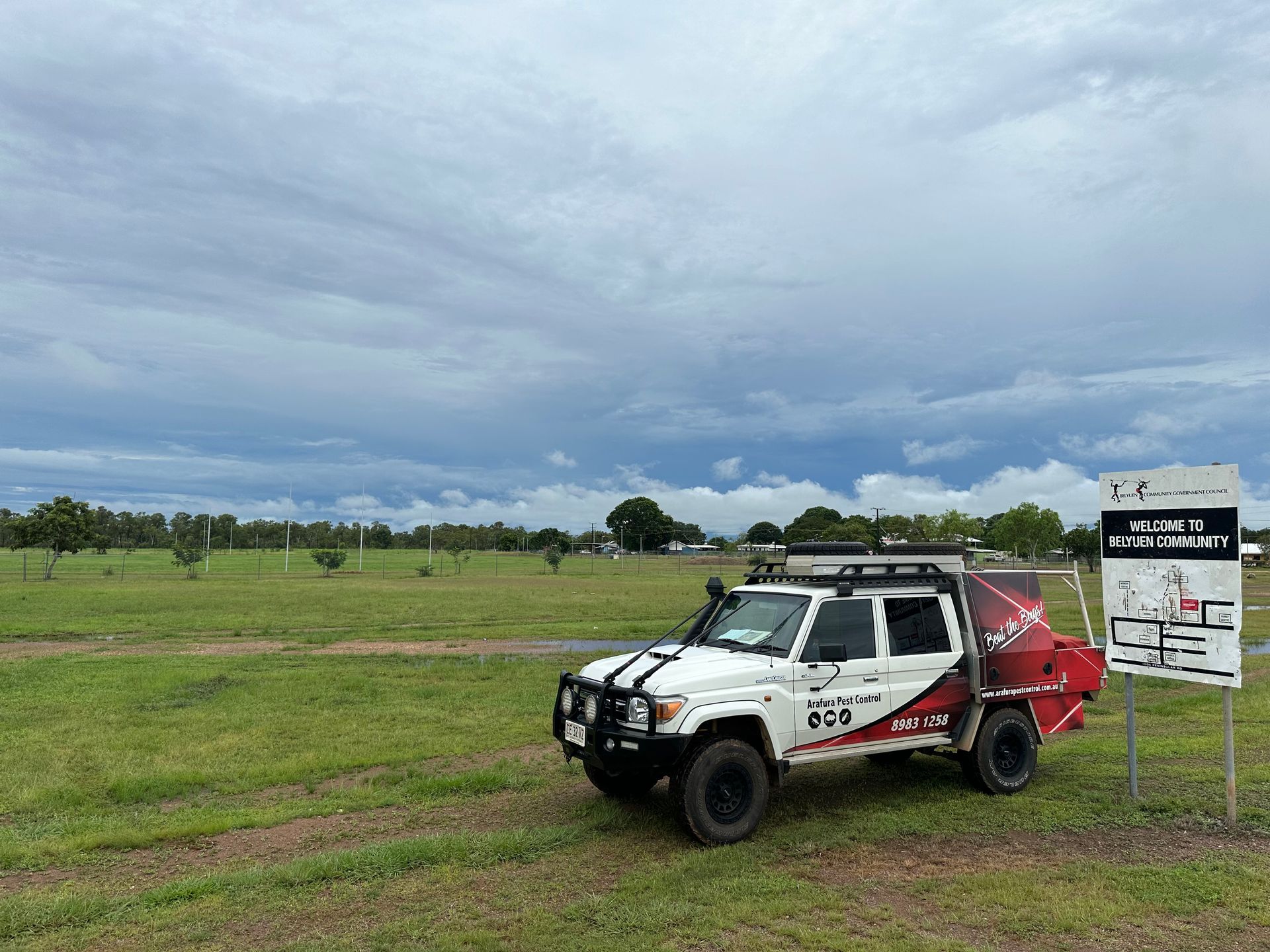 A white truck is parked in a grassy field next to a sign.