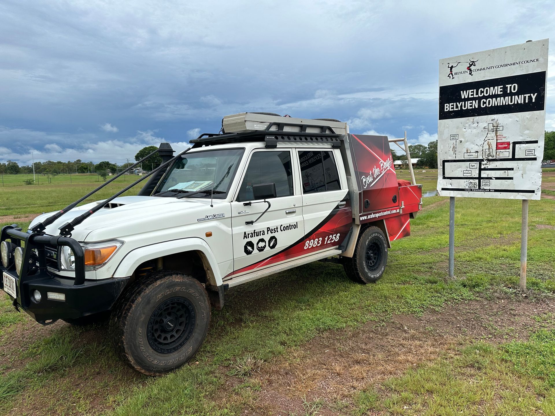 A white truck is parked in a grassy field next to a sign.