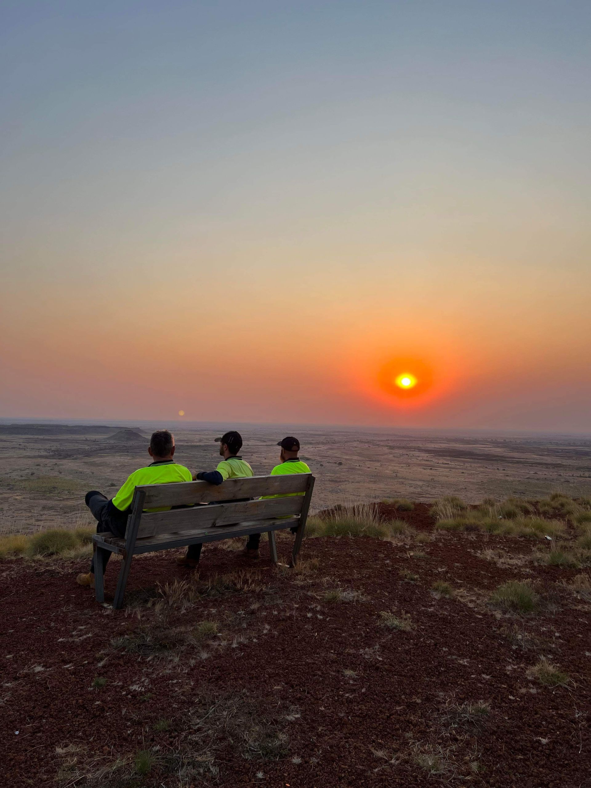 Three people are sitting on a bench watching the sunset.