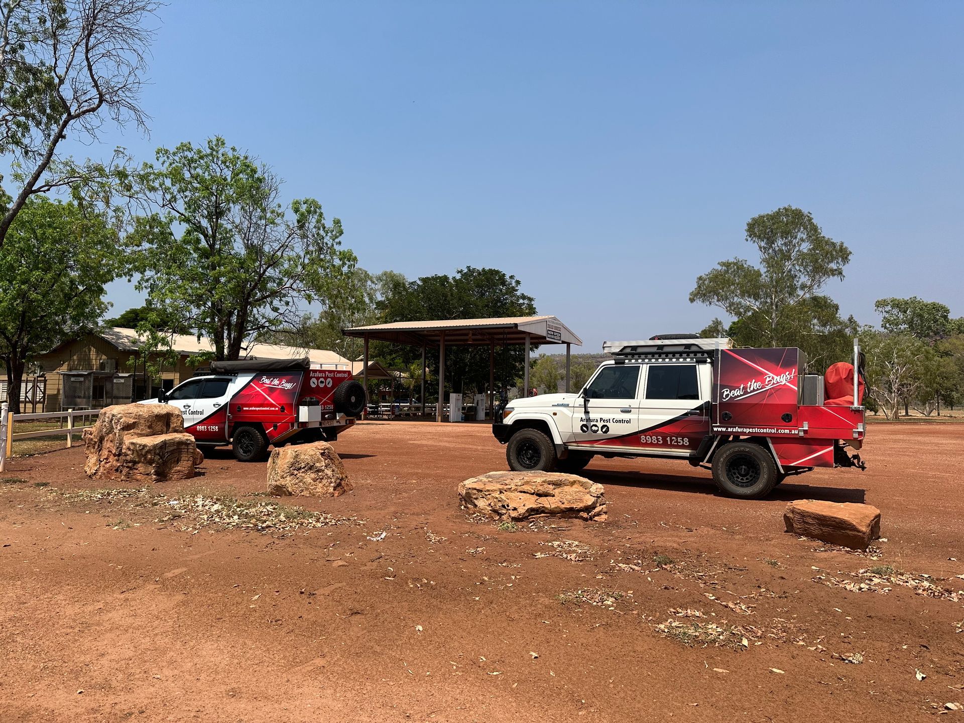 Two red and white trucks are parked in a dirt field.