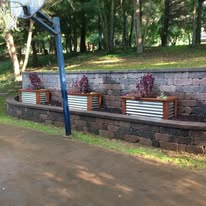 Basketball hoop and three planters built into a retaining wall in a grassy yard.