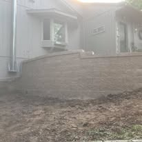 Exterior of a house with a retaining wall and dirt ground.