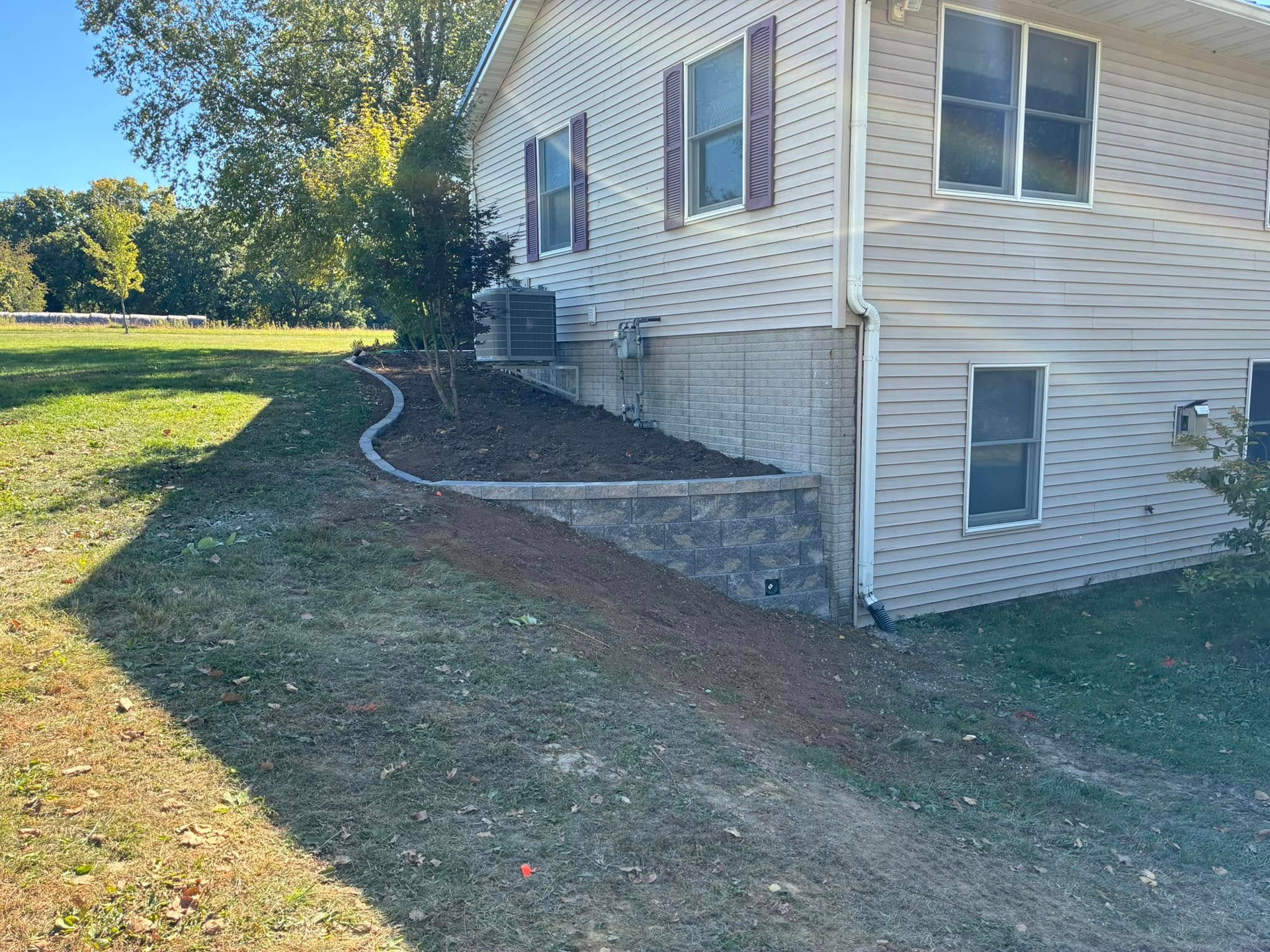 Exterior of a house with a retaining wall and dirt ground.
