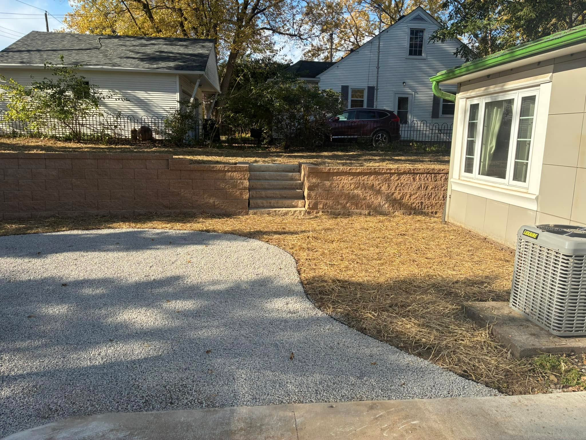 Circular concrete patio in yard, near house and retaining wall; lamp post.