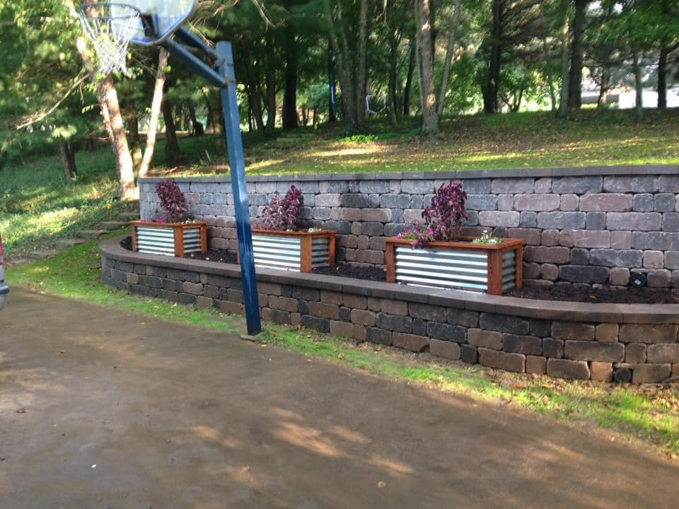 Basketball hoop and three planters built into a retaining wall in a grassy yard.
