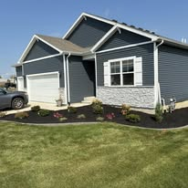 Blue-sided house with white trim, garage, and flower bed. Green lawn in front.