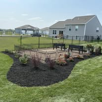 Backyard with benches, black fence, and garden bed in front of a house on a sunny day.