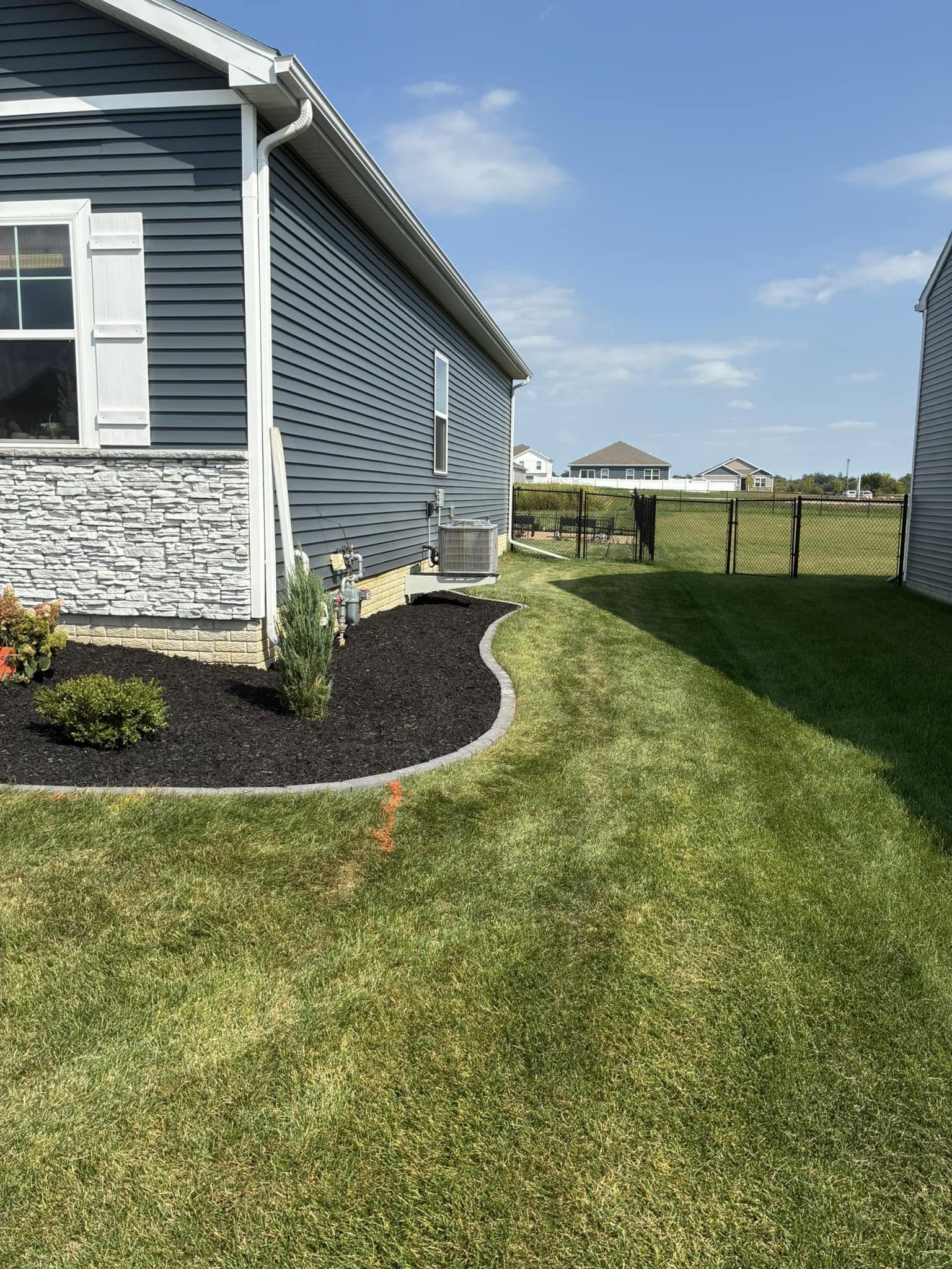 Blue house with black mulch landscaping, green grass, and a fence.