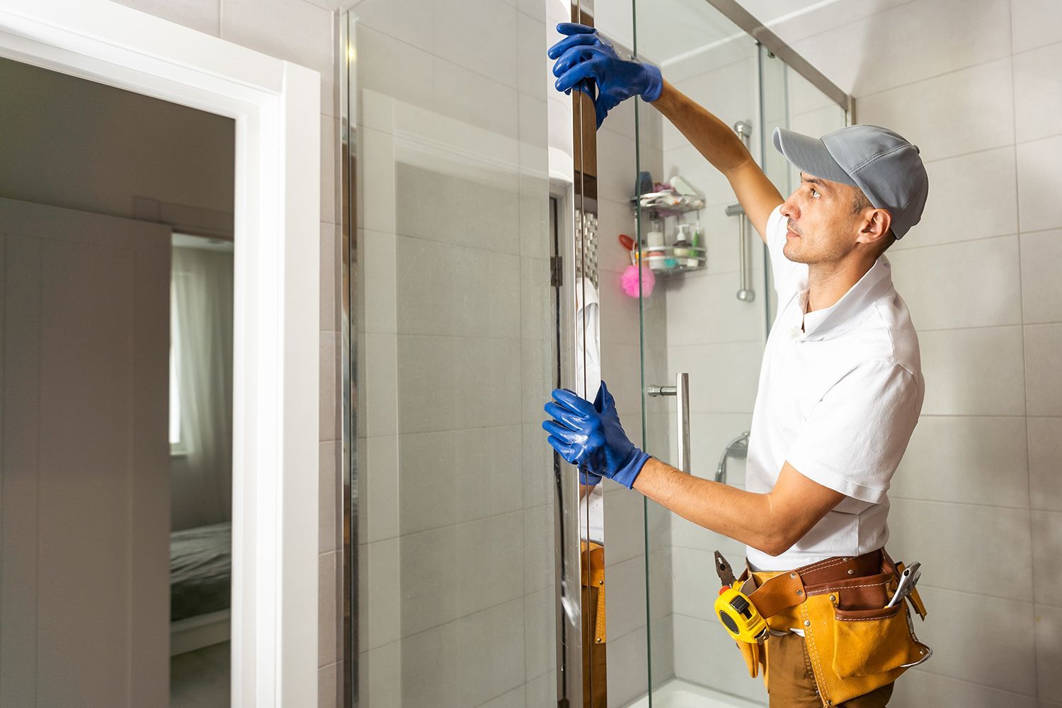 Installer fitting a frameless glass shower door in a modern tiled bathroom.