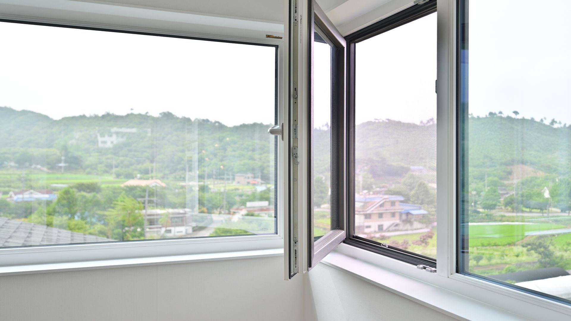 Open insulated window with double-pane glass overlooking a green landscape.