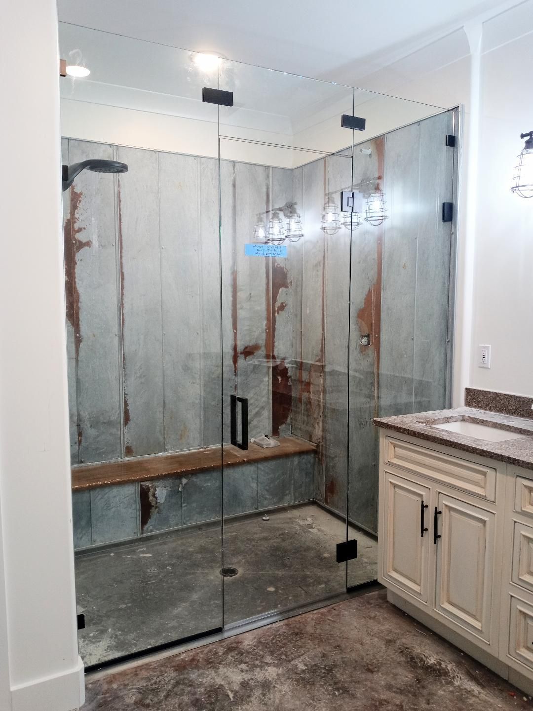 A bathroom with a glass shower enclosure and distressed wood-look walls. A vanity with a stone countertop is in the corner.