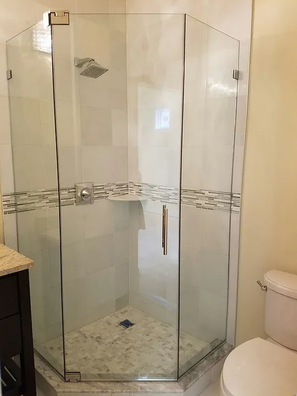 A clear, multi-sided glass shower enclosure in a bathroom with a tiled base and a decorative band.