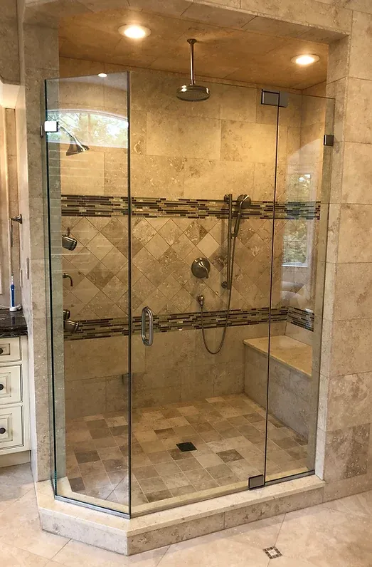 A spacious, luxurious shower with glass doors, beige tiles, and multiple showerheads. A built-in bench is visible inside.