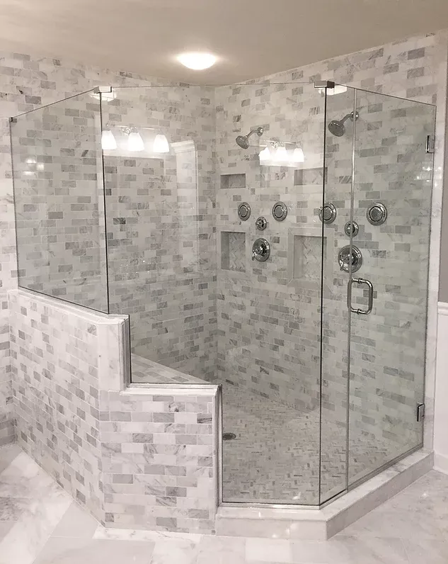 A luxurious walk-in shower with gray and white tile, a built-in bench, and glass doors. Multiple showerheads and controls are visible.