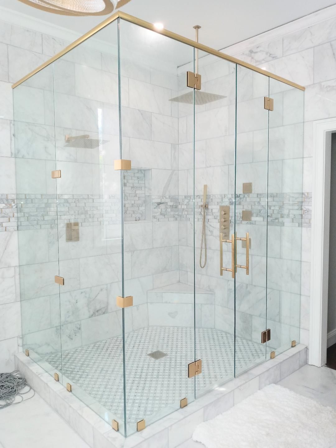 A luxurious walk-in shower with clear glass walls and gold hardware. The walls are marble, and the shower floor has patterned tiles.