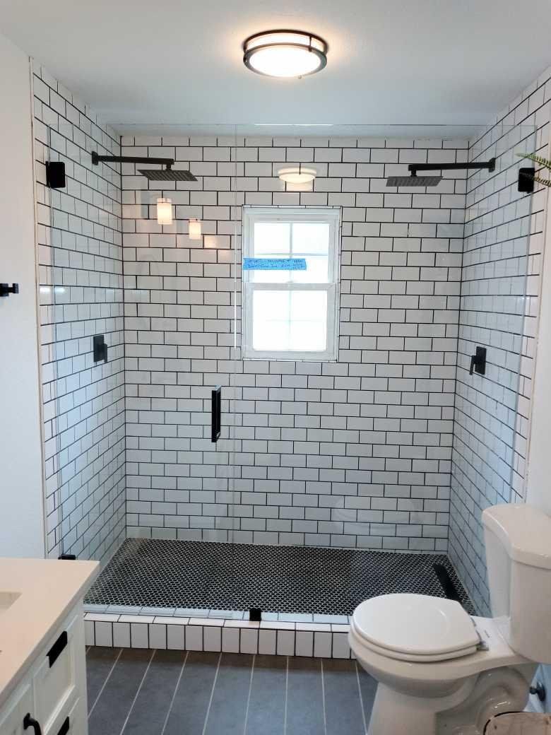 Modern white-tiled bathroom with black accents, a shower with glass doors, a window, and a toilet.
