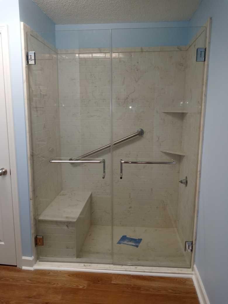 Glass shower enclosure with a built-in bench and grab bars, installed within a bathroom with light blue walls.