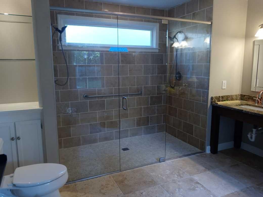 A modern bathroom with a tiled shower, glass doors, and a toilet. Beige tiles and a vanity with a brown countertop are also visible.