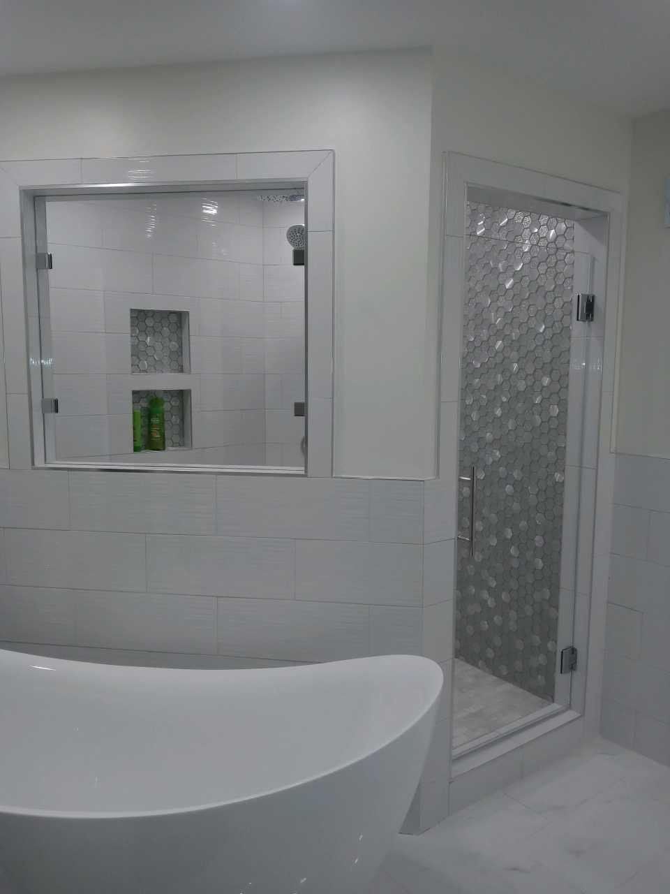 Modern bathroom with a white bathtub, shower with textured glass, and a recessed shelf with toiletries.