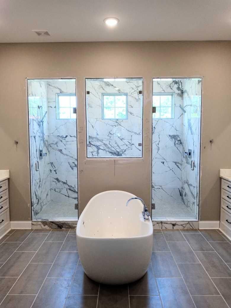 Modern bathroom with a freestanding egg-shaped tub centered in front of three glass-enclosed showers with marble tile.