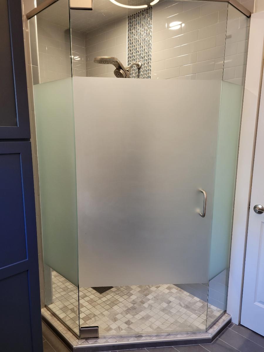 A glass-enclosed shower with frosted glass panels and a mosaic tiled floor. It has a showerhead and handle.