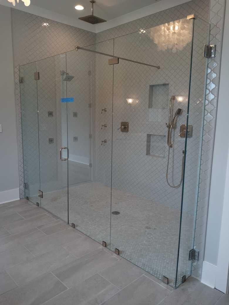 A large glass shower enclosure with a glass door and multiple shower heads, against a light gray tile background.