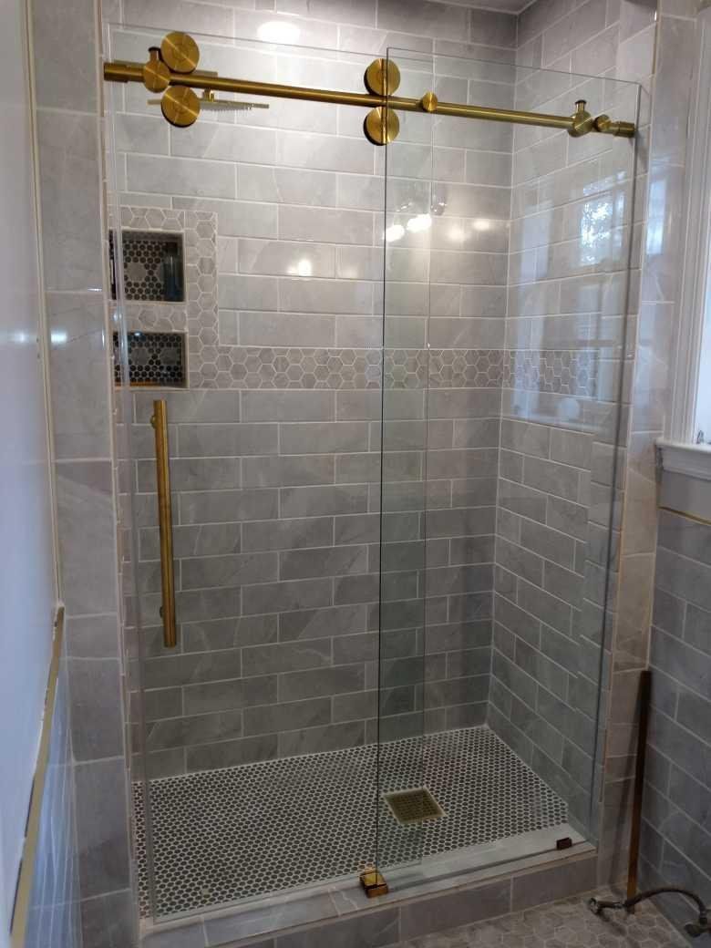 Shower with gray tile walls, a clear glass door with gold-colored hardware, and a patterned floor.