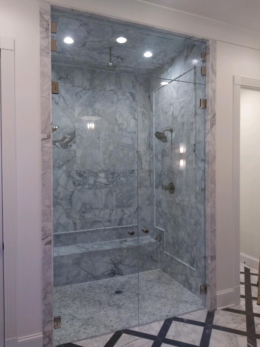 A luxury shower with marble walls and glass doors. Two shower heads and a built-in bench are visible.