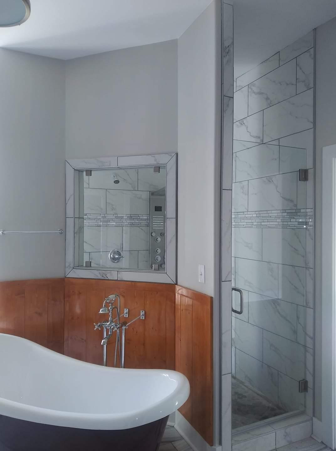 A bathroom with a white clawfoot tub, glass shower, and a marble-tiled wall. The walls are gray and have wood paneling.