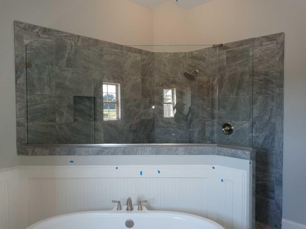 Bathroom with a gray marble-tiled shower enclosure, a white bathtub, and a white wainscoting.