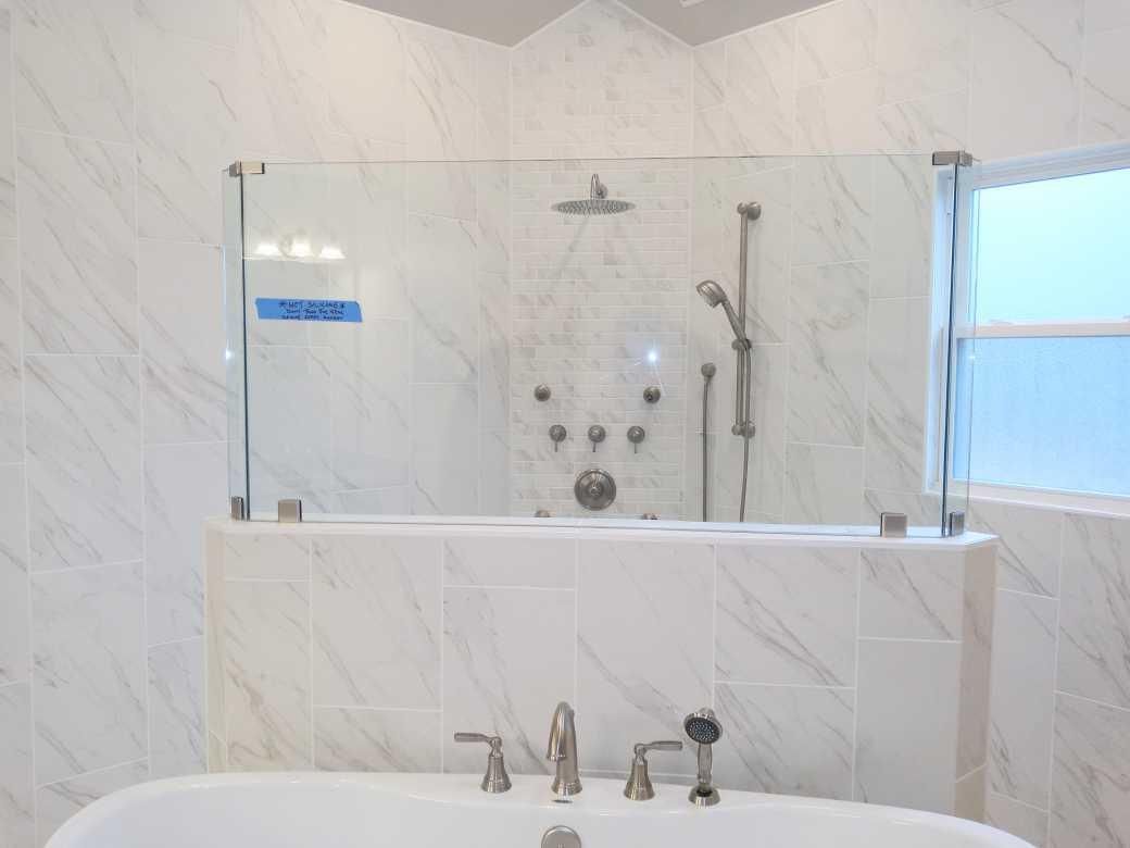 White marble bathroom with a glass shower screen above a bathtub. Showerhead and jets are visible.