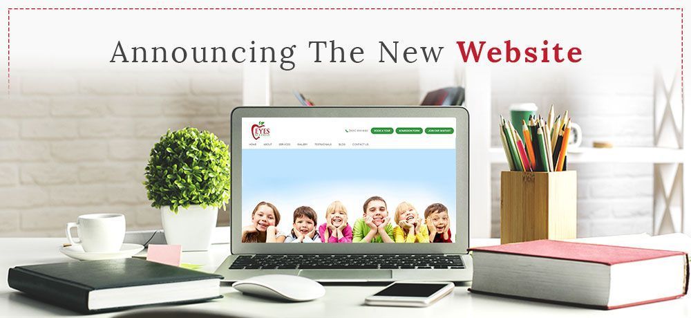 Laptop displaying new website with photo of children; desk with coffee, books, and pens.