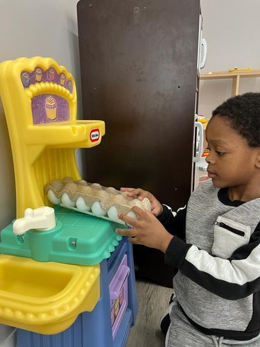 A young boy playing with a toy kitchen set, holding an egg carton.