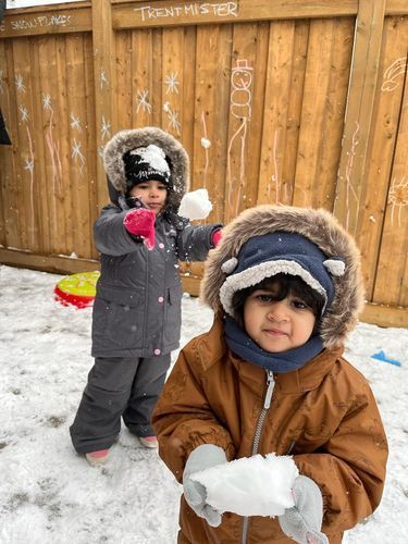 Two children in winter coats play in the snow. One throws a snowball, the other holds one.